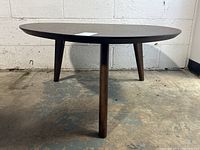 Front view of mid-century modern style coffee table with dark brown wooden triangular rounded top and three tapered legs.