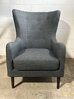 Front view of grey wingback chair showing tufted back and dark wood legs