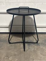 Front view of the round black metal table with a handle on top, showing the table's overall shape and leg design.