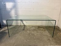 Front view of clear glass waterfall coffee table against cinder block wall