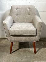 Front view of grey lounge chair showing upholstery, cushion, armrests, and tapered wooden legs.