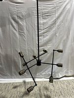 Full view of the modern black metal hanging ceiling light fixture suspended vertically, showing the eight bulb sockets spread on horizontal and diagonal arms.