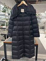 Full front view of black Moncler coat on hanger