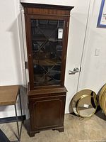 Front view of tall narrow walnut cabinet showing full height and glass-paned door