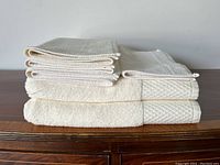 Six cream colored cotton towels stacked, showing bath towels at bottom and smaller towels on top