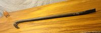 Long metal crow bar with flat and curved ends on a wooden surface.