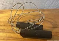 Clear cable jump rope with black foam handles laid on wooden surface showing the entire rope and handles.