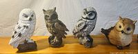 Four resin owl sculptures on display showing different colors and styles.