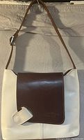 Front view of two-tone leather handbag with brown flap and cream body, adjustable strap hung for display.