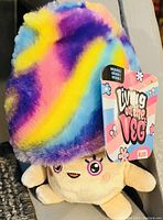 Photo shows a plush mushroom toy with a beige stem and vibrant rainbow colored fuzzy cap. The toy has embroidered facial features and an attached colorful brand tag reading 'Living on the Veg' and 'Russ'.