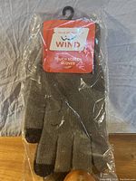 Photo of the full pair of brown knit gloves with black tips on thumb and index finger still in original plastic packaging with attached Wind brand tag.
