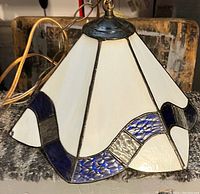 Close-up photo of a stained glass hanging light showing its white and blue textured glass panels and brass hanging chain.