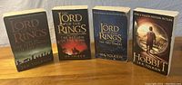 Photo showing four paperback books laid out side-by-side on a wooden surface. From left to right: The Lord of the Rings: The Fellowship of the Ring, The Lord of the Rings: The Return of the King, The Lord of the Rings: The Two Towers, and The Hobbit with a major motion picture cover.