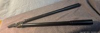 Black metal tree clippers laid flat showing long handles and jointed cutting blades.