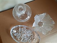 Photo showing four glass dishes: one round clipped-flower edge dish, one oval embossed fruit dish, one fluted round dish, and one round glass bowl with a hollow center base (likely the cake stand base).