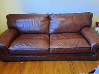 Front view of the brown leather couch highlighting the seating cushions and dark brown piping along the edges.