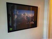 Framed photo featuring clouds in sky with visible reflections on glass, hung on wall.