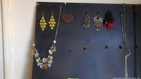 Photo of several pairs of earrings and a large statement necklace displayed on a black board.