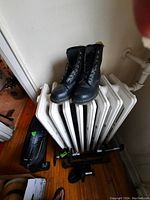 Pair of black Dr. Martens boots sitting on a white radiator, showing front and side profile.