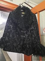 Front view of black brocade jacket with large faux wool collar and cuffs showing button closure and fabric pattern.