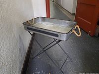 Galvanized metal butler's tray with rope handles on a folding metal stand, showing front and side views.