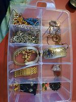 Top-down photo of compartmentalized jewelry box with earrings, bracelets, necklaces and a wristwatch visible.