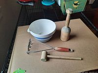 Overhead view of the blue-striped lipped bowl with a wooden pestle, a wooden mallet, and a metal masher with a wooden handle on cardboard.