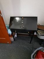 Front view of the closed secretary desk showing the slant top with a decorative brass handle and two brass knobs on the drawer beneath.