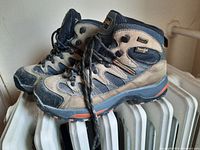 Left side view of right hiking boot showing blue and beige color, lace hooks, SympaTex branding, and tread detail.