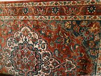 Close-up photo of the rug showing the floral medallion pattern in rust, cream, and green hues.