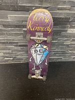 Front view of the used Baker skateboard featuring a purple deck, Terry Kennedy name, and a diamond character graphic, with attached trucks and wheels.