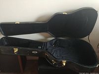 Open guitar case showing padded black interior and interior storage compartment.