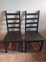 Front view of two dark brown IKEA Kaustby chairs side by side on carpeted floor against plain wall.