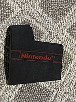 Front view of black plastic NES dust cover with red Nintendo logo on carpet background.