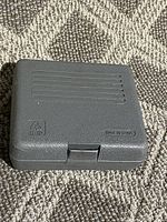Closed gray plastic storage case for handheld nut driver tool, shown on carpet.