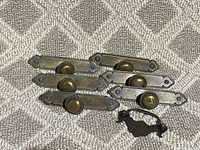 Six vintage metal drawer handles with oval brass knobs displayed on a textile surface.