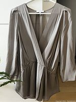 Front view of beige silk blouse showing deep V-neck, crossover design, 3/4 sleeves, and cinched waist detail on hanger.