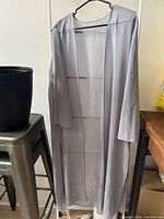 Full view of the light grey chiffon cardigan hanging on a black hanger, showing its length and open front.