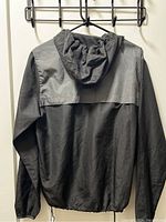 Back view of the black Billabong windbreaker jacket showing hood, gray yoke, and elastic hem with adjustable drawstring.