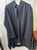 Front view of black blazer hanging on hanger showing oversized fit and single button clasp.