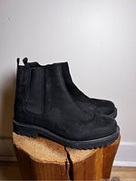 Side profile of black suede Chelsea boots on wooden surface.
