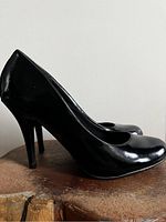 Side profile view of one black pump showing shiny patent leather and high stiletto heel.