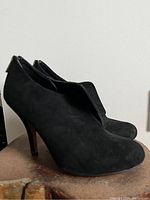 Pair of black suede booties positioned to show outer sides and heel zipper detail.