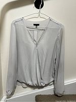 Full view of white Dynamite blouse hanging on hanger, showing elasticized cuffs and front trim detail.