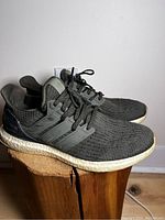 Side view of greenish-grey Adidas Ultra Boost sneakers showing knit upper, black heel counter and Boost white midsole.