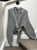 Grey knit wrap sweater hanging on a hanger showing full front view with long puff sleeves and ribbed cuffs.