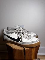 Pair of men's Nike sneakers, white with black swoosh, side view showing wear and gum sole.