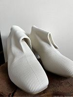 Front and side views of the pair of white knit ankle booties, showing ribbed knit texture and block heels.