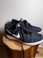 Side view of Nike women's Lunarlon Flyknit sneakers showing black and purple knit pattern with white swoosh logo, white sole, and black laces.