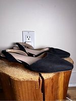 Side angle photo showing full profile of pointed black ballet flats on a wooden surface against a white wall and electrical outlet.